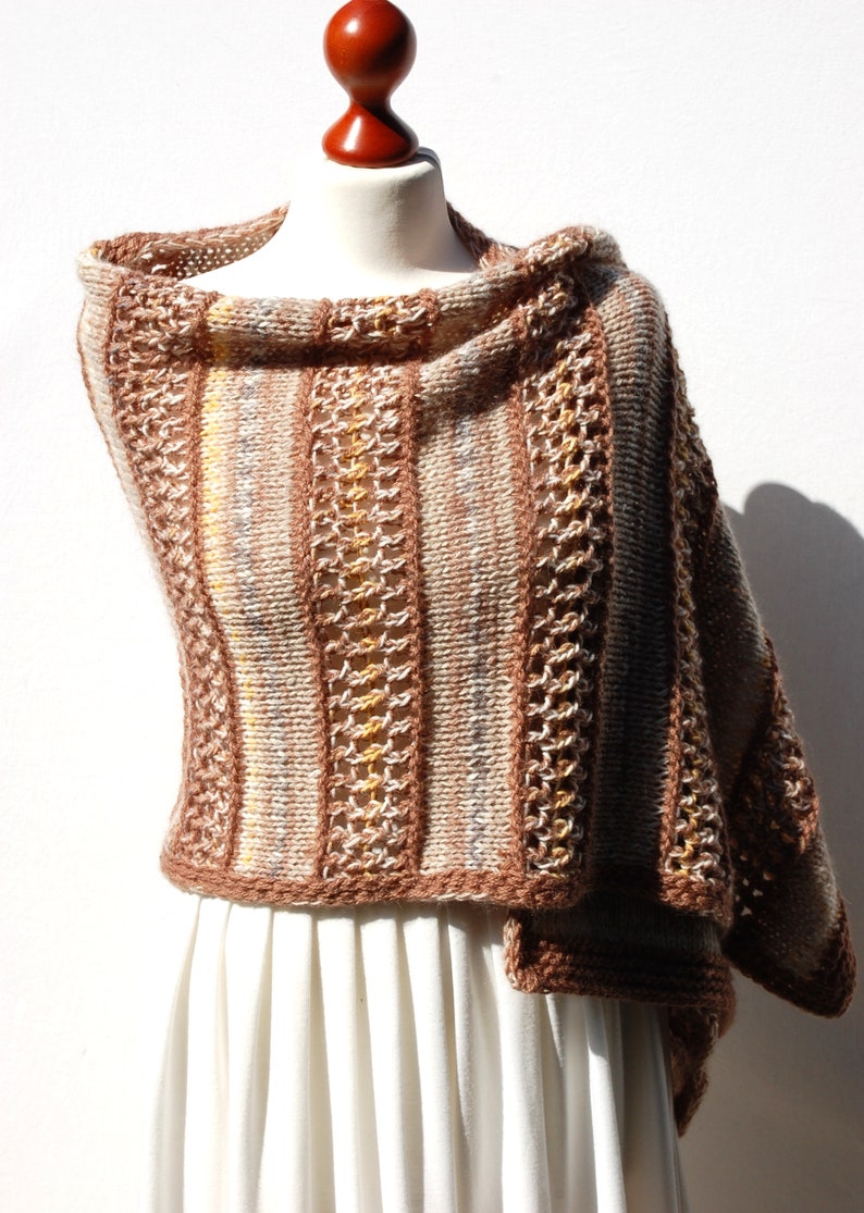 May include: A brown and beige knitted shawl with a striped pattern and a crocheted border. The shawl is draped over a white dress form.