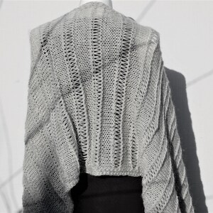 May include: A gray knitted shawl with a delicate openwork pattern. The shawl is draped over a mannequin and has a loose, flowing silhouette.