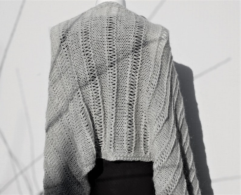 May include: A gray knitted shawl with a delicate openwork pattern. The shawl is draped over a mannequin and has a loose, flowing silhouette.