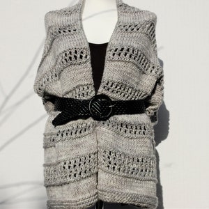 May include: A gray knitted cardigan with a open front and a black belt. The cardigan has a textured knit pattern with a lace-like design.