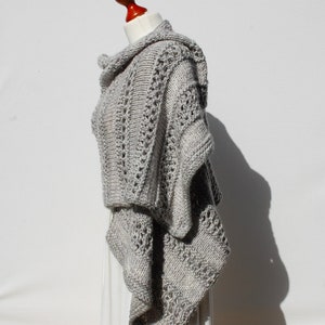 May include: A gray knitted poncho with a cowl neck and a lacy pattern. The poncho is draped over a mannequin.