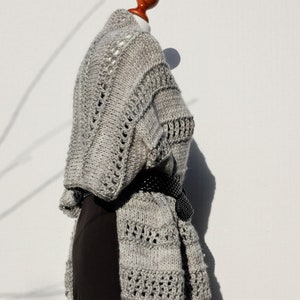 May include: A gray knitted cardigan with a delicate openwork pattern. The cardigan is draped over a mannequin and has a black belt.