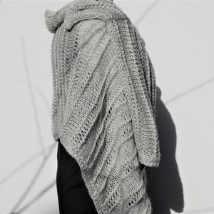 May include: A gray knitted shawl with a diagonal pattern. The shawl is draped over a person's shoulders and is made of a soft, lightweight yarn.