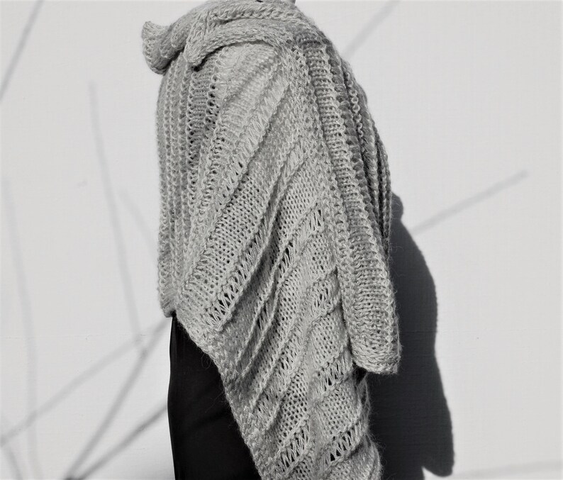 May include: A gray knitted shawl with a diagonal pattern. The shawl is draped over a person's shoulders and is made of a soft, lightweight yarn.