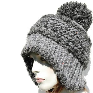 May include: A grey and black fuzzy knit hat with a pom pom on top. The hat has a long flap that can be pulled down to cover the ears.