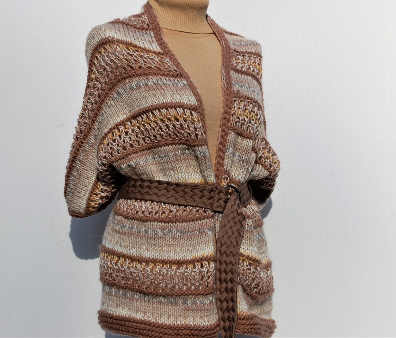 May include: A brown, white, and beige striped knitted cardigan with a brown braided belt. The cardigan has a V-neck and long sleeves.