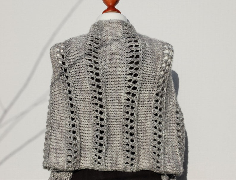 May include: A gray knitted vest with a lacy pattern. The vest has a high neckline and a loose fit.