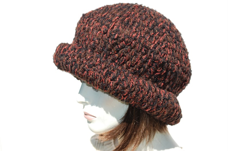Puede incluir: Un gorro de punto marr&oacute;n y naranja con un ala ancha. El gorro est&aacute; hecho de un hilo suave y texturizado.