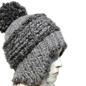 May include: A grey knitted hat with a large pom-pom on top. The hat has a fold-down ear flap design.