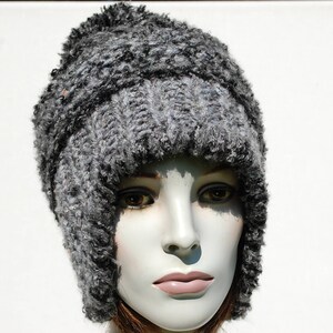 May include: A grey knitted hat with a thick, fuzzy texture. The hat has a wide brim and covers the ears.