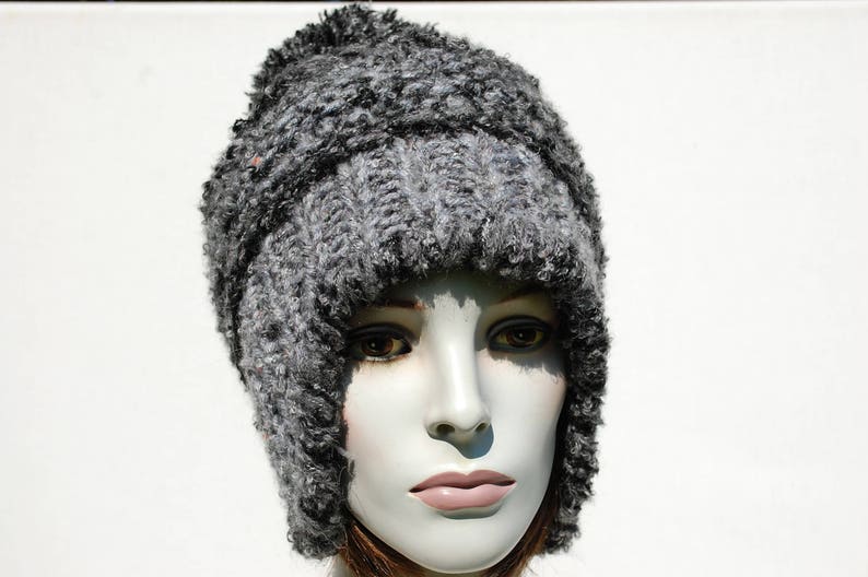 May include: A grey knitted hat with a thick, fuzzy texture. The hat has a wide brim and covers the ears.