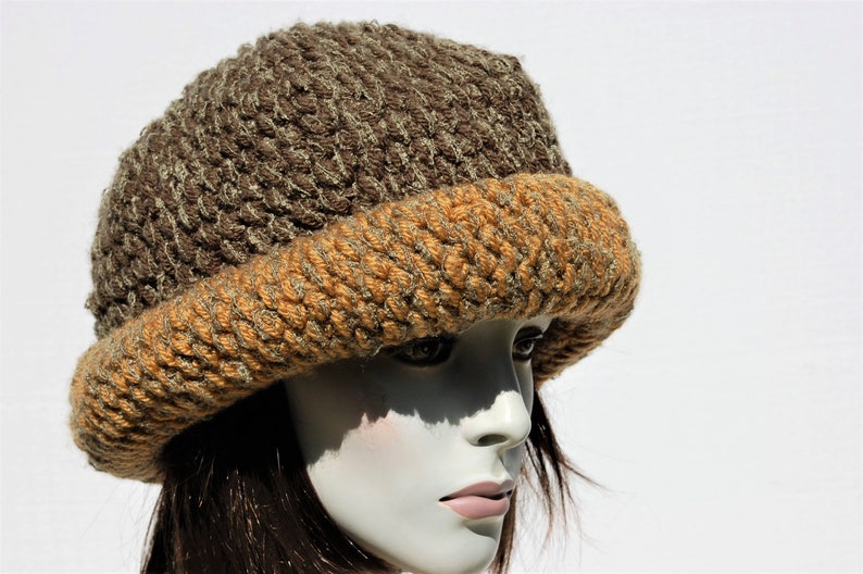 Puede incluir: Un gorro de punto marr&oacute;n y naranja con un ala ancha.