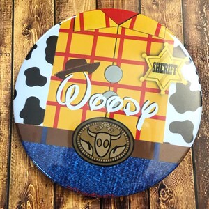 May include: A round button with a cartoon image of Woody from Toy Story. Woody is wearing his signature cowboy hat, vest, and jeans. The button has the word "Woody" written in white cursive letters. The button also has a sheriff's star badge with the word "Sheriff" written on it.