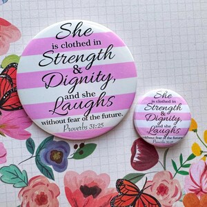 May include: Two pink and white striped round buttons with the text "She is clothed in Strength & Dignity, and she Laughs without fear of the future. Proverbs 31:25" in black text.