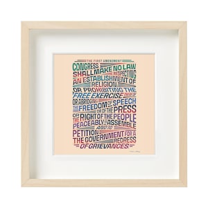 May include: Framed print of the First Amendment text in various colors. The text includes phrases like "Congress shall make no law" and "freedom of speech." The frame is light wood.