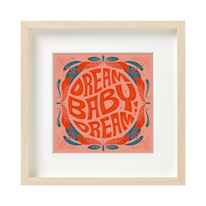 May include: A framed print with a peach background and a teal and red circular design. The text inside the circle reads "Dream Baby Dream".
