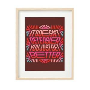 May include: Framed motivational poster with a red, pink, and blue color scheme. The poster features the text "It doesn't get easier, you just get better."