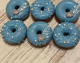 Puede incluir: Seis donas redondas con un glaseado azul claro suave. Cada dona está decorada con finos hilos de glaseado azul, pequeñas perlas de azúcar blancas y un adorno de fondant gris con forma de elefante en algunas de las donas del conjunto.
