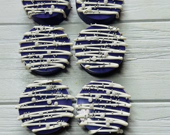 May include: Six round, purple-coated treats arranged in two columns. Each treat is decorated with horizontal white icing drizzles, small silver metallic sprinkles, and larger white spherical sugar pearls scattered across the top surface.