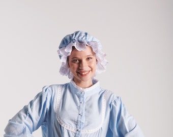Puede incluir: Una mujer con un camisón azul claro con ribetes de encaje blanco y un gorro a juego de encaje azul claro y blanco.