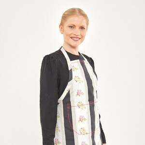 Könnte beinhalten: Eine schwarz-weiß gestreifte Schürze mit Blumenmuster und einem Rüschen-Saum. Die Schürze hat eine große Tasche auf der Vorderseite.