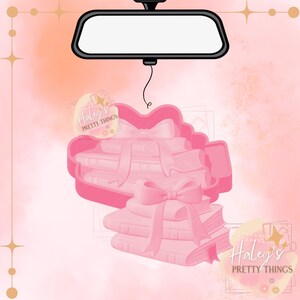 Könnte beinhalten: Rosa Ausstecher in Form eines Autos mit einem Stapel Bücher und einer Schleife. Das Bild enthält auch einen Rückspiegel und den Text "Haley's Pretty Things". Der Hintergrund ist eine Aquarellwaschung in Rosa und Pfirsich.