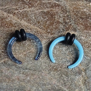 May include: Two blue glass septum rings with black silicone o-rings. The rings are in the shape of a crescent moon.
