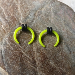May include: Two neon green acrylic ear cuffs with black o-rings. The cuffs are shaped like a crescent moon.