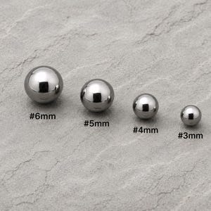 Puede incluir: Cuatro esferas de metal de color plateado pulido dispuestas en fila de mayor a menor. Las esferas están etiquetadas con texto que indica sus diámetros como #6mm, #5mm, #4mm y #3mm, representando sus tamaños en milímetros.