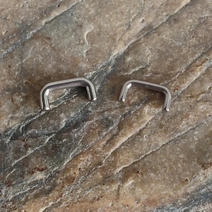 Pode incluir: Dois anéis de prata sem costura para piercings corporais. Os anéis são de tamanhos diferentes, com o anel maior à esquerda e o anel menor à direita.