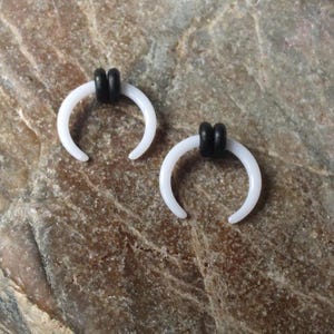 May include: Two white acrylic horseshoe shaped earrings with black o-rings.