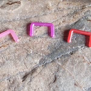 May include: Three plastic nose rings in different colors: pink, purple, and red. The rings are all the same size and shape, and they are all made of a clear plastic material.