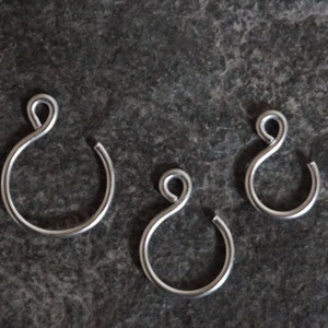 Puede incluir: Tres anillos de metal plateado con un bucle en la parte superior. Los anillos son de diferentes tamaños.