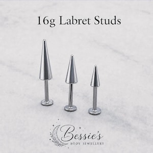 May include: Three silver-colored metal labret studs with cone-shaped ends of varying heights, arranged in a row. The text 16g Labret Studs is visible at the top, and the logo for Bessie's Body Jewellery is printed at the bottom of the image.