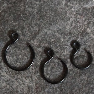 Puede incluir: Tres anillos de cortina de metal negro de diferentes tamaños. Los anillos son redondos con un pequeño bucle en la parte superior.