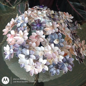 May include: A bouquet of seashell flowers in shades of pink, purple, and white. The flowers are arranged in a dome shape and are made from various types of seashells.