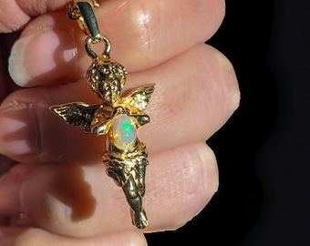 May include: A gold angel pendant with a white opal gemstone in its hands. The pendant is on a gold chain.