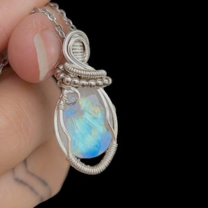 Peut inclure: Un collier pendentif en argent avec une pierre précieuse irisée en forme de goutte d'eau. La pierre est sertie dans un délicat sertissage en fil de fer. Le pendentif est suspendu à une fine chaîne en argent, créant un bijou élégant.