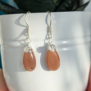 May include: A pair of silver dangle earrings with teardrop-shaped sunstone stones.