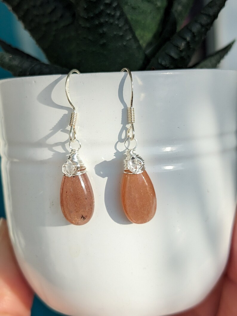 May include: A pair of silver dangle earrings with teardrop-shaped sunstone stones.