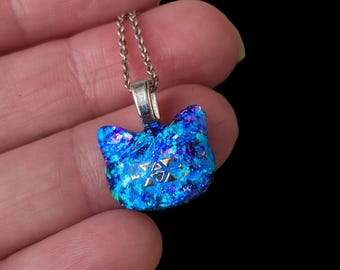 May include: A blue and purple glass cat head pendant with silver glitter and a silver chain. The pendant features a silver star design in the centre.