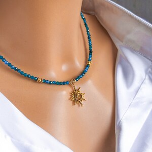 May include: A gold sun pendant necklace with a blue gemstone bead chain. The necklace is on a white mannequin.