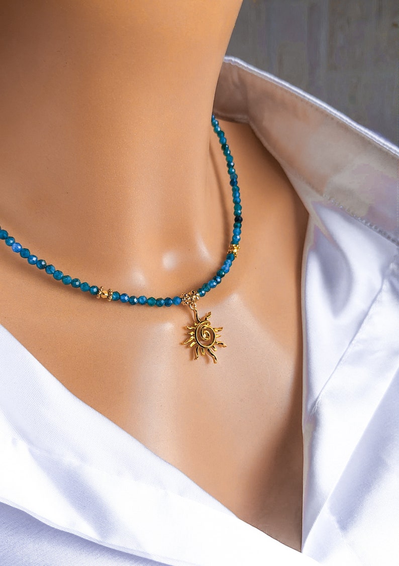 May include: A gold sun pendant necklace with a blue gemstone bead chain. The necklace is on a white mannequin.