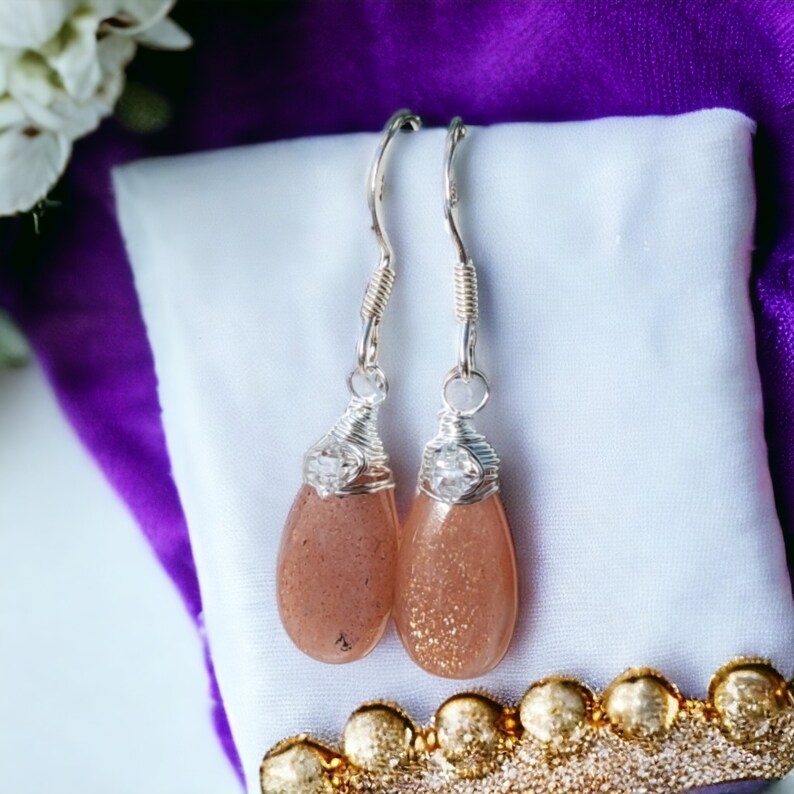 May include: A pair of silver dangle earrings with teardrop-shaped sunstone stones and clear crystal accents.