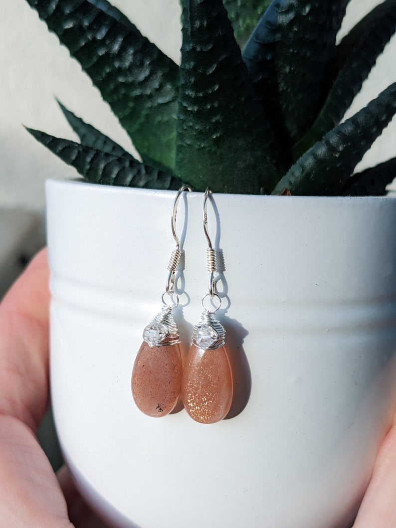 May include: A pair of silver wire wrapped earrings with teardrop shaped sunstone stones and clear crystal accents.