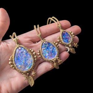 Puede incluir: Tres collares de oro con colgantes de lágrima de resina azul e iridiscente. Cada colgante tiene detalles dorados y un dije con una luna creciente, una pluma y una estrella.