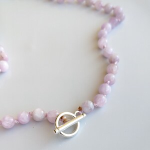 May include: A light purple beaded necklace with a silver toggle clasp. The necklace features round, polished beads strung together. The clasp is a simple, elegant design.