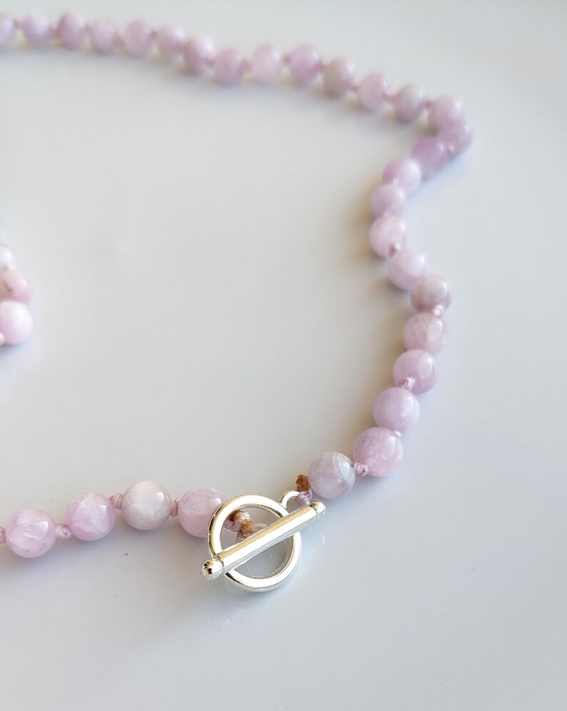 May include: A light purple beaded necklace with a silver toggle clasp. The necklace features round, polished beads strung together. The clasp is a simple, elegant design.