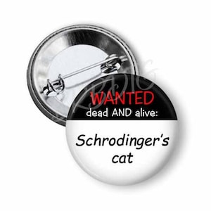 May include: A black and white button with the text "WANTED dead AND alive: Schrodinger's cat" in red and black lettering.