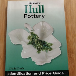 May include: A green book titled "Warman's Hull Pottery Identification and Price Guide" by David Doyle. The cover features a white ceramic dish with green grapes and leaves.